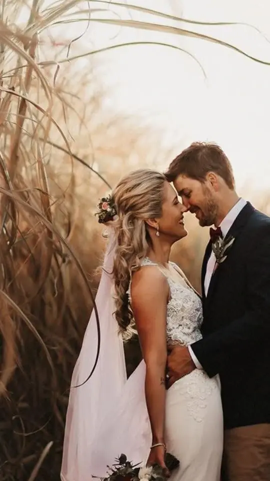 Bride wearing a curled half-up wedding hairstyle with a floral hairpiece beside the groom