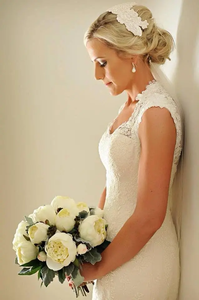 Bride with a lace-pinned blonde updo holding a white peony bouquet